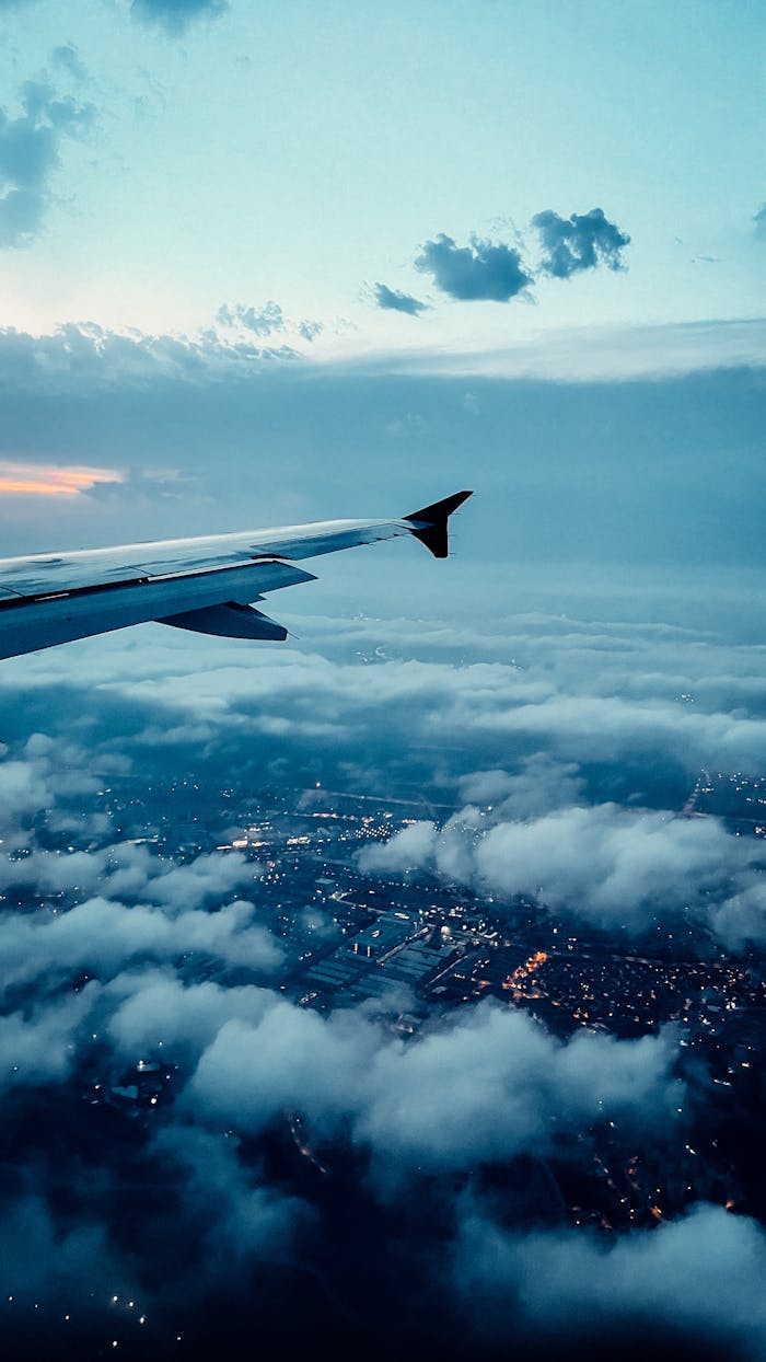 A stunning aerial view from an airplane window, showcasing clouds and city lights below.