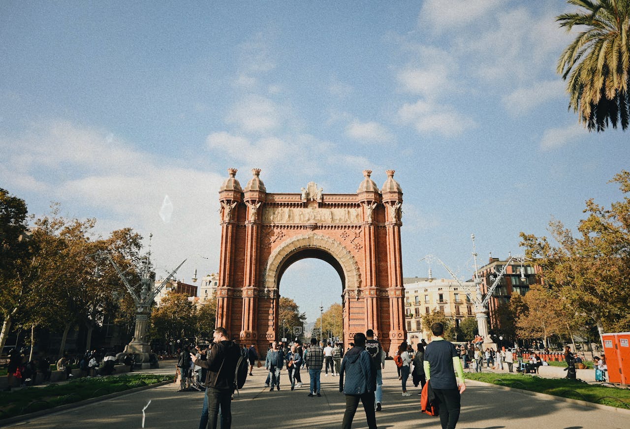 People walking near Arc de Triomf in Barcelona with clear skies overhead.
